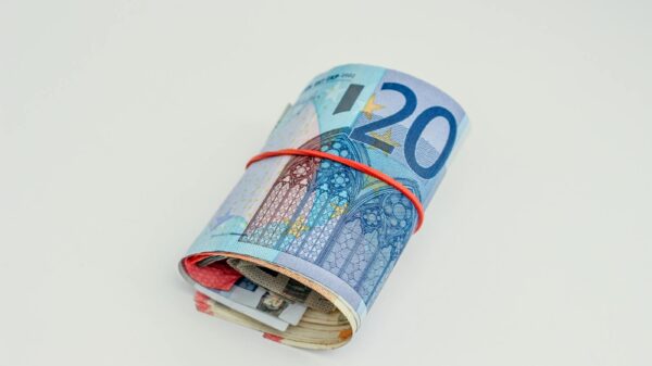 Close-up of rolled euro banknotes secured with a red rubber band on white background.