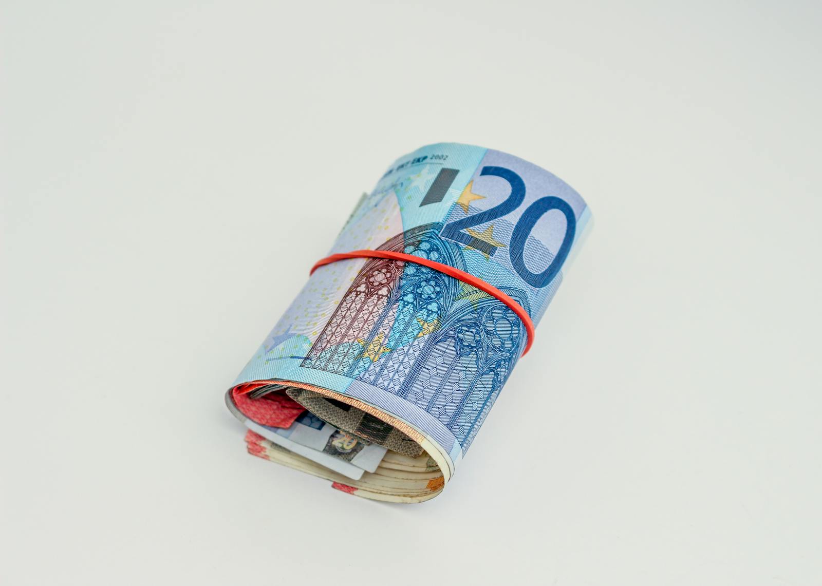Close-up of rolled euro banknotes secured with a red rubber band on white background.