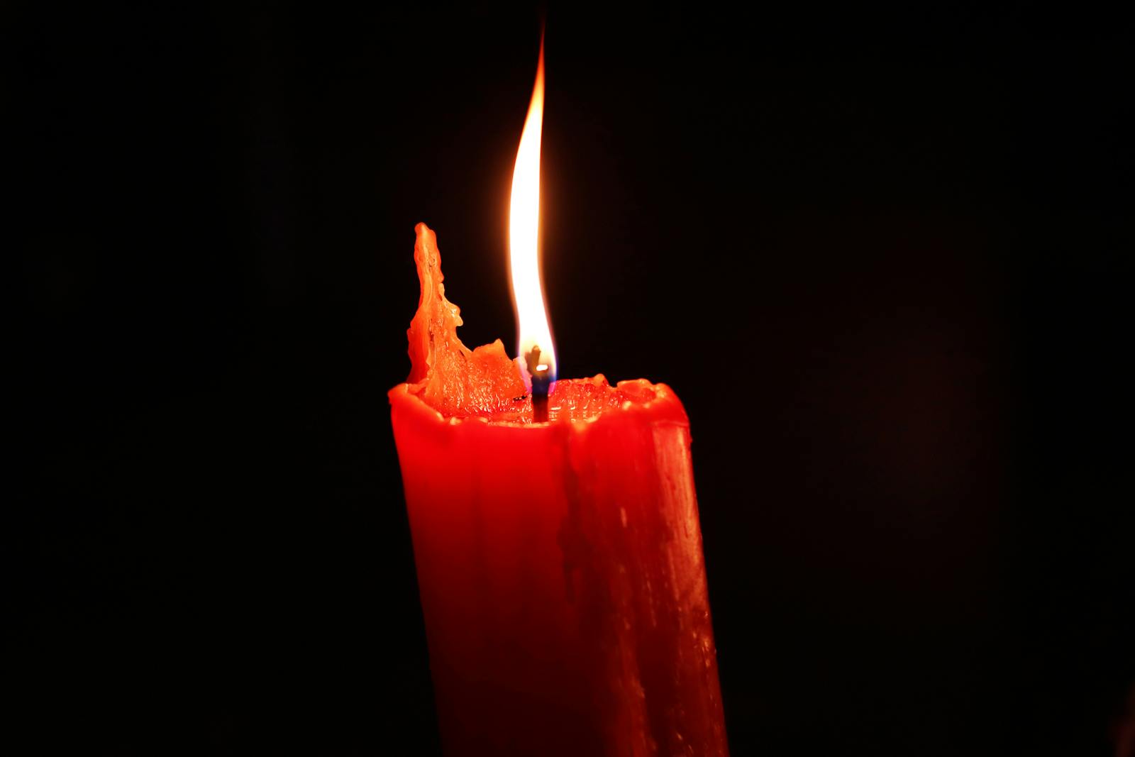 Close-up of a burning red candle glowing in the dark, symbolizing warmth and hope.