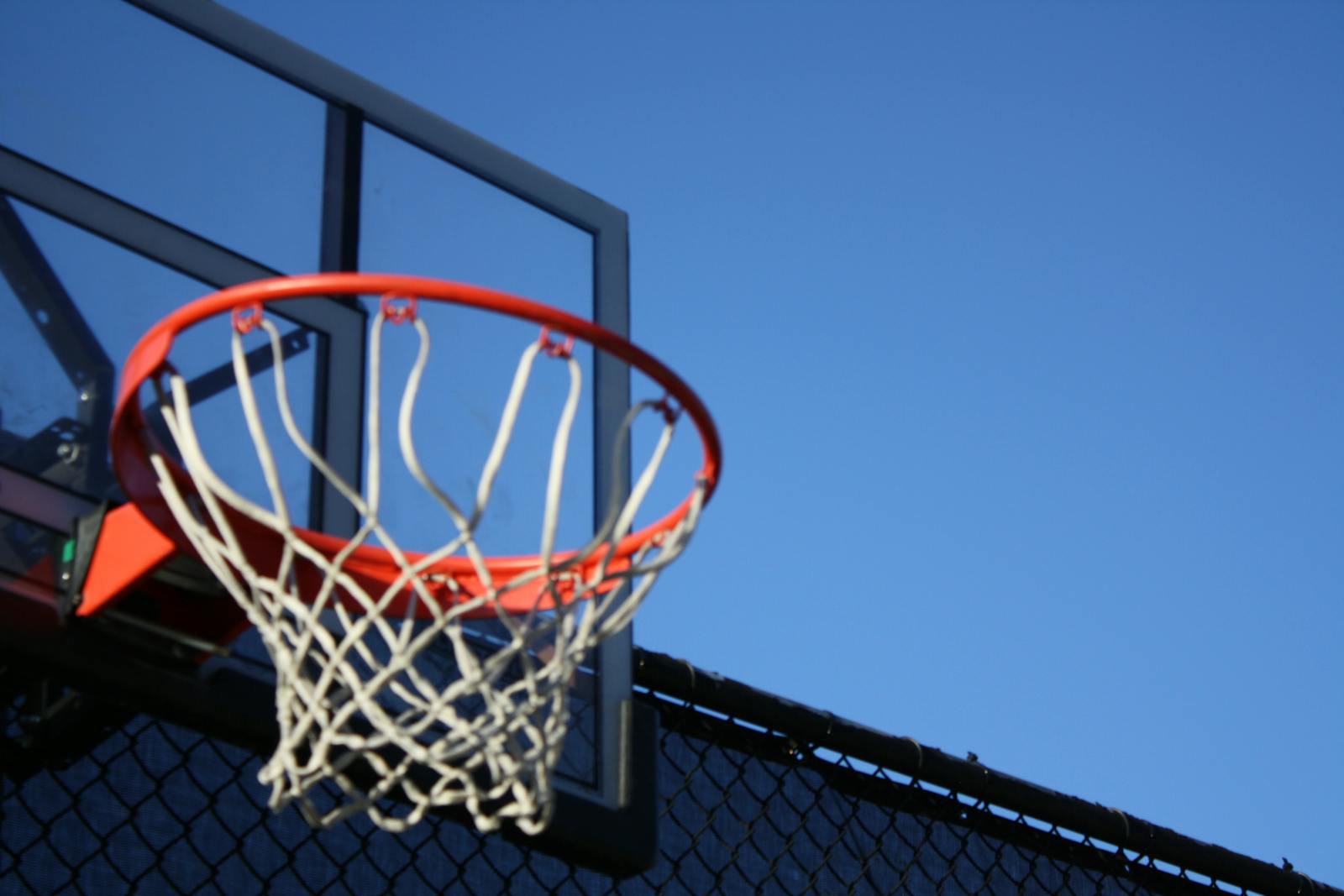 A vibrant outdoor basketball hoop with net set against a clear blue sky, ideal for sports visuals.