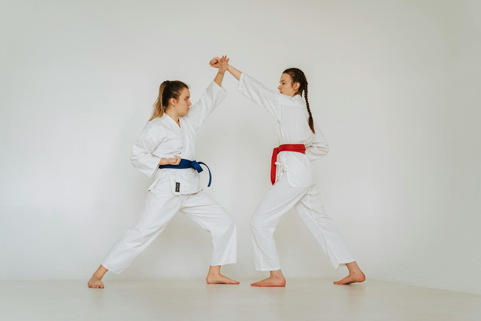 Two women engage in martial arts training, wearing traditional karate uniforms indoors.