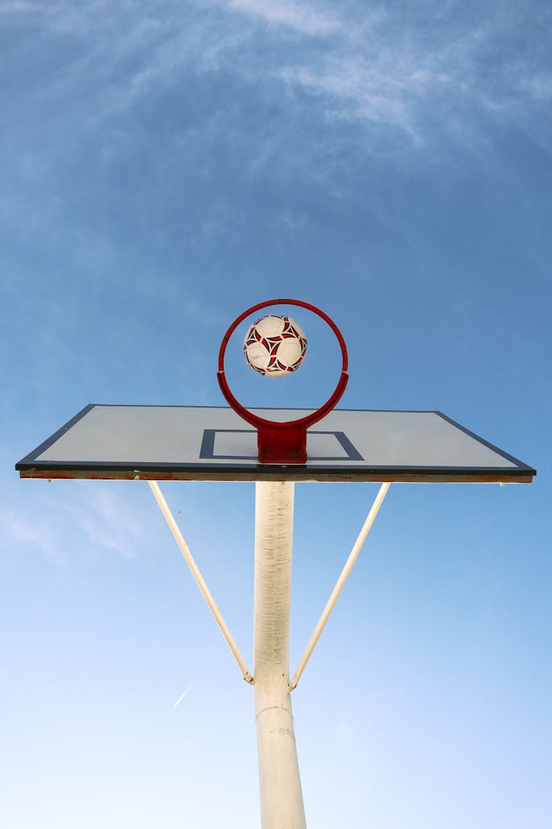 A soccer ball perfectly positioned in a basketball hoop against a clear sky, symbolizing achievement.