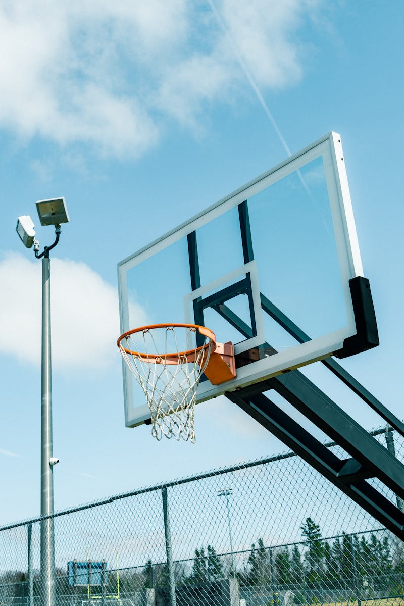 Outdoor basketball hoop with backboard under a clear blue sky, perfect for sports and recreation themes.