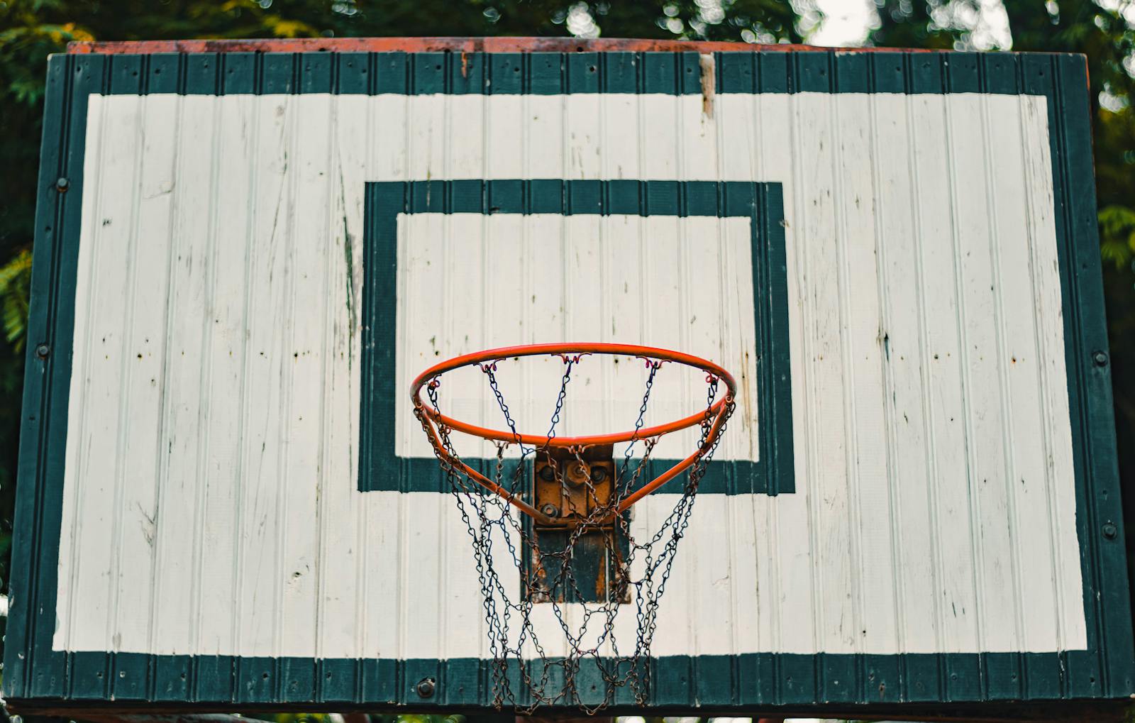 A rustic basketball hoop with a weathered backboard outdoors.