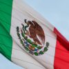 Brightly colored Mexican flag waving against a clear blue sky, symbolizing patriotism and freedom.