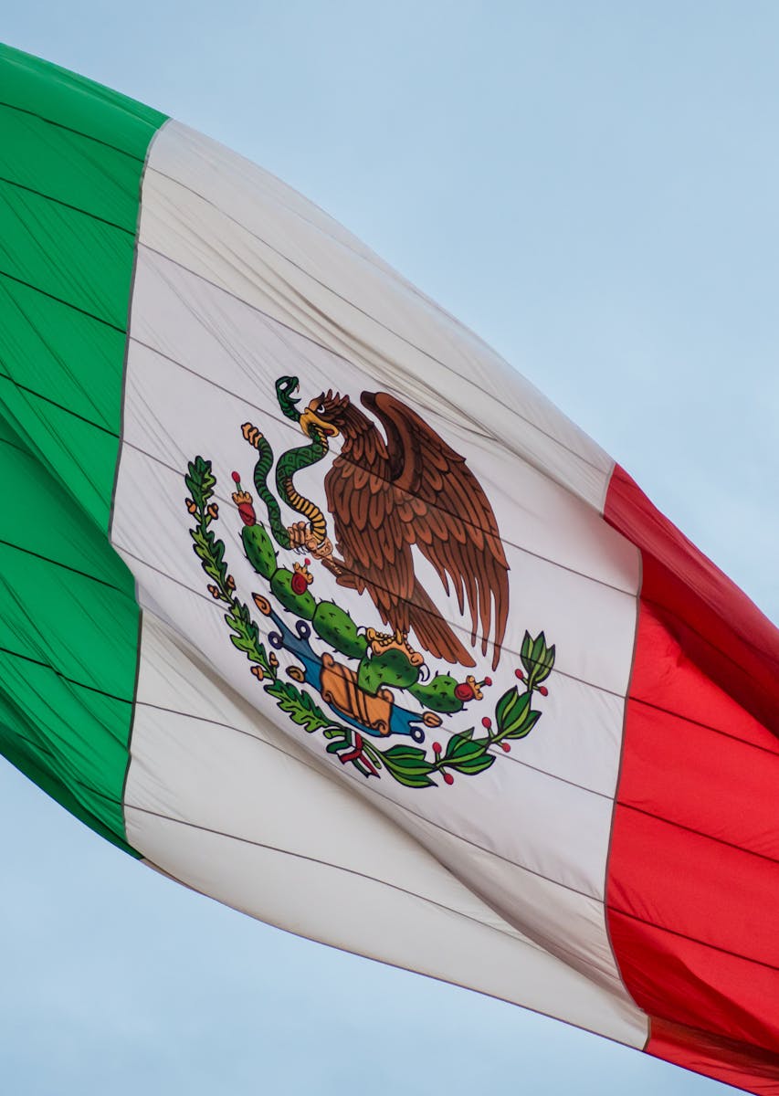 Brightly colored Mexican flag waving against a clear blue sky, symbolizing patriotism and freedom.