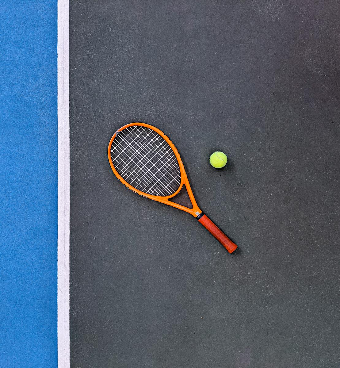 A tennis racket and ball on a court, emphasizing sports equipment essentials.