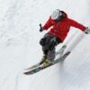 A skier in a red jacket descends a steep snowy slope, showcasing skill and adventure in winter sports.