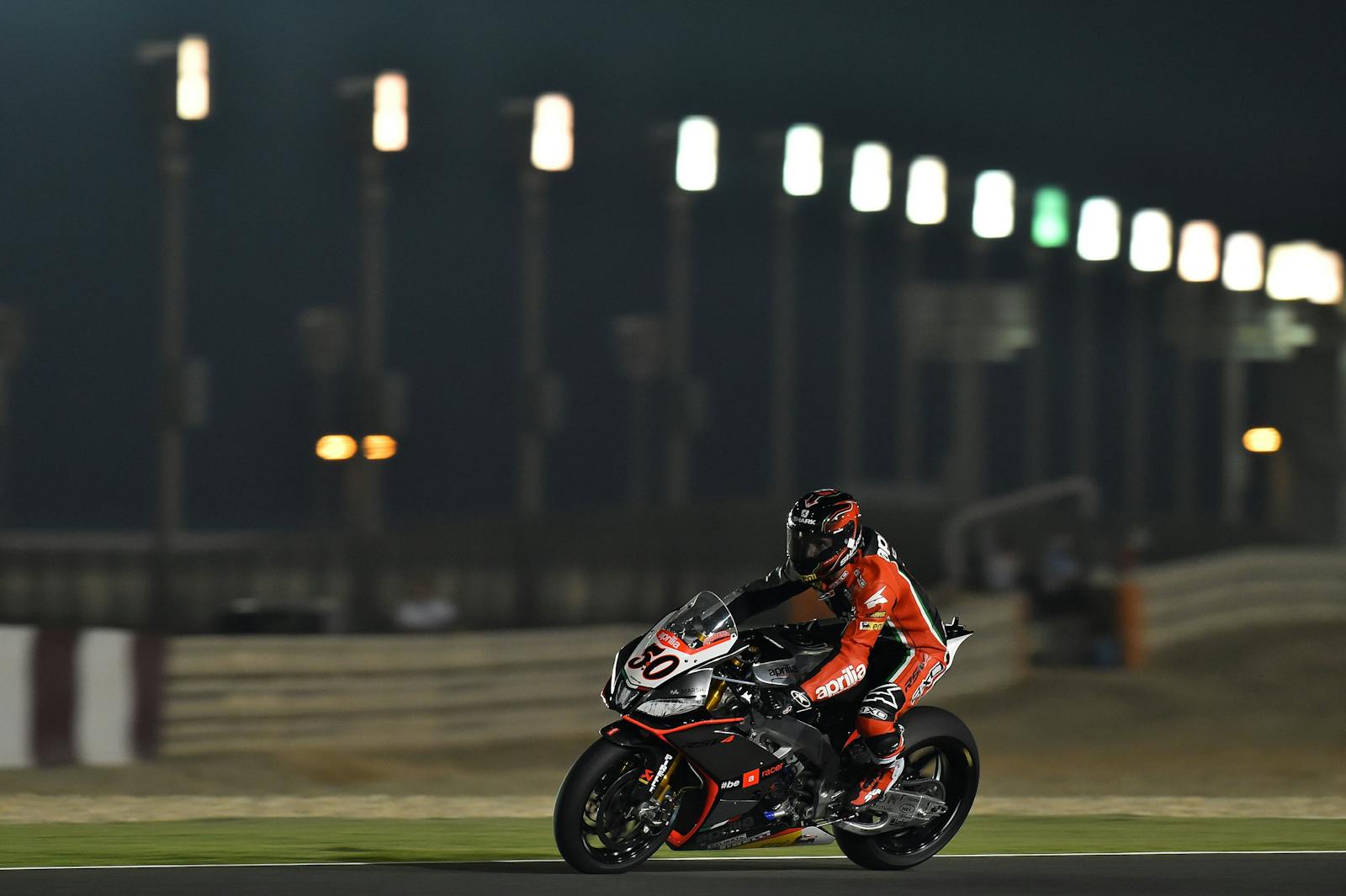 Motorcycle racer in action on the track at night, showcasing speed and skill under stadium lights.