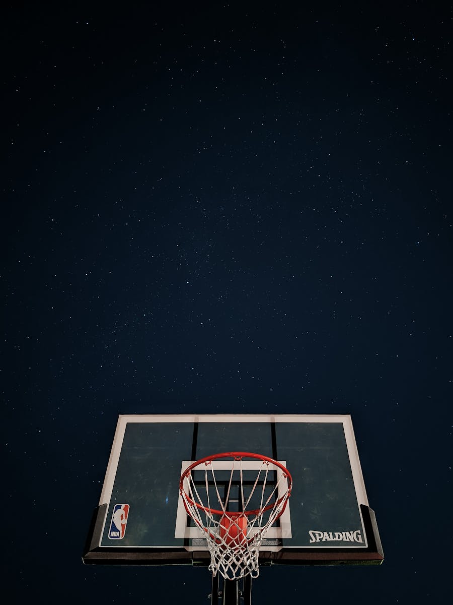A basketball hoop silhouetted against a dark night sky filled with stars.