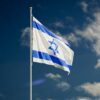 The Israeli national flag waving against a clear blue sky with clouds.