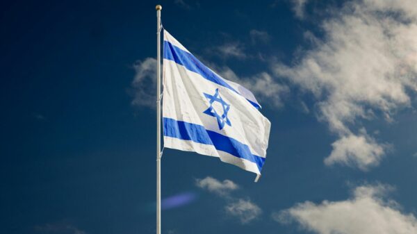 The Israeli national flag waving against a clear blue sky with clouds.