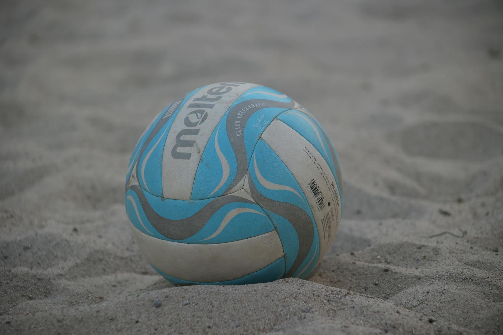 A close-up of a colorful beach volleyball resting on sand.