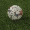 A detailed vertical shot of a weathered soccer ball resting on lush green grass.