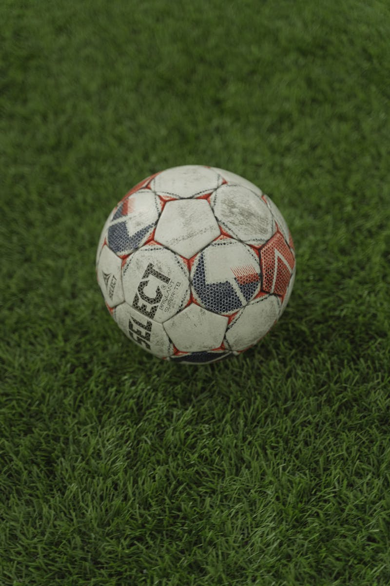 A detailed vertical shot of a weathered soccer ball resting on lush green grass.