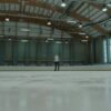 A solitary figure stands confidently on an indoor ice rink, ready for skating.
