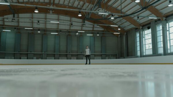 A solitary figure stands confidently on an indoor ice rink, ready for skating.