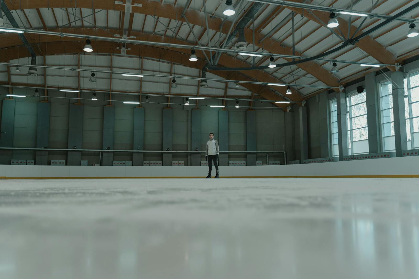 A solitary figure stands confidently on an indoor ice rink, ready for skating.