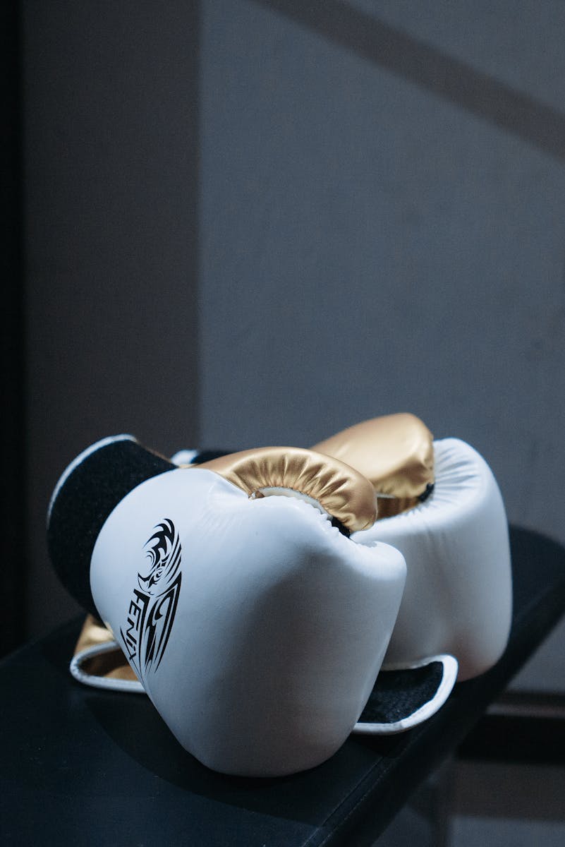 White and gold boxing gloves resting elegantly on a black surface, highlighting their premium quality.