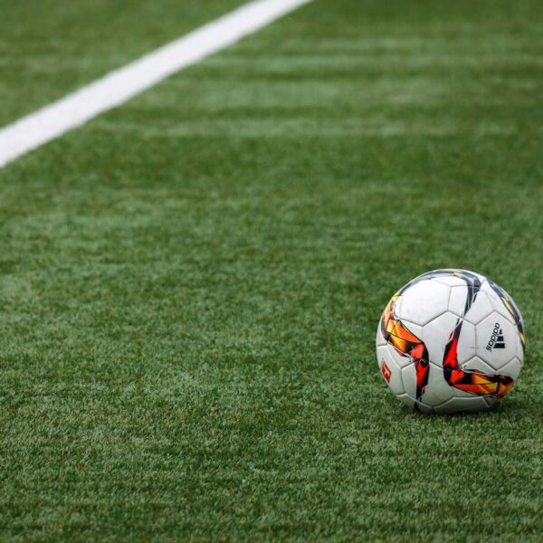 A vibrant soccer ball resting on a pristine grass field beside a white sideline.