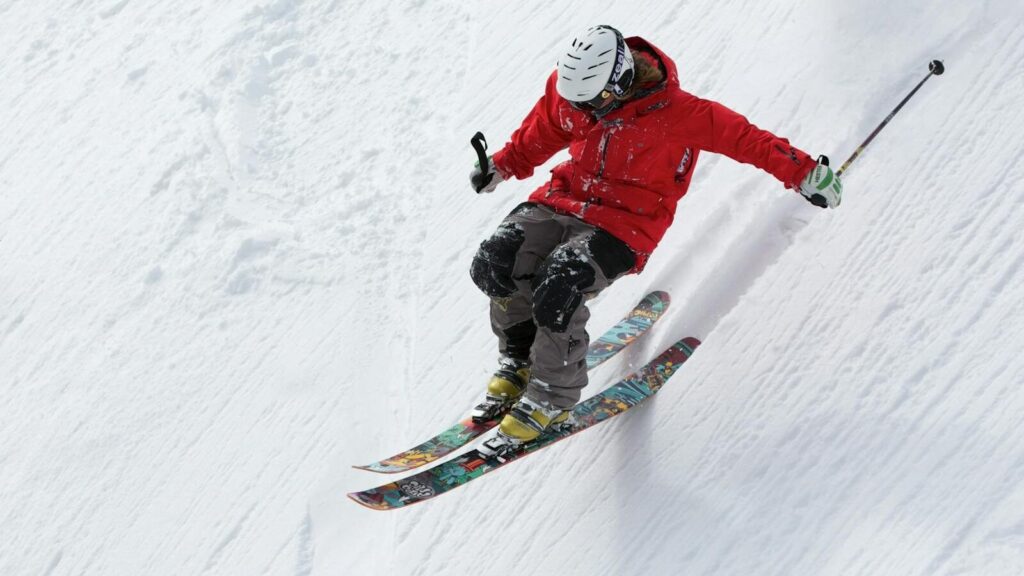 A skier in a red jacket descends a steep snowy slope, showcasing skill and adventure in winter sports.