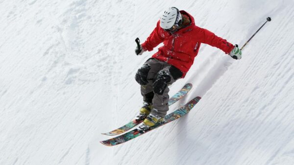 A skier in a red jacket descends a steep snowy slope, showcasing skill and adventure in winter sports.