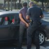 A police officer arrests a suspect standing near a car outdoors.