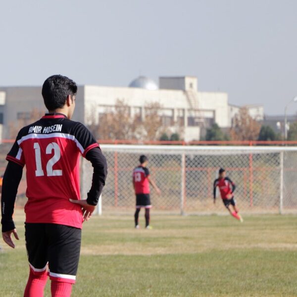 man in blue and red soccer jersey shirt and black shorts standing on green grass field