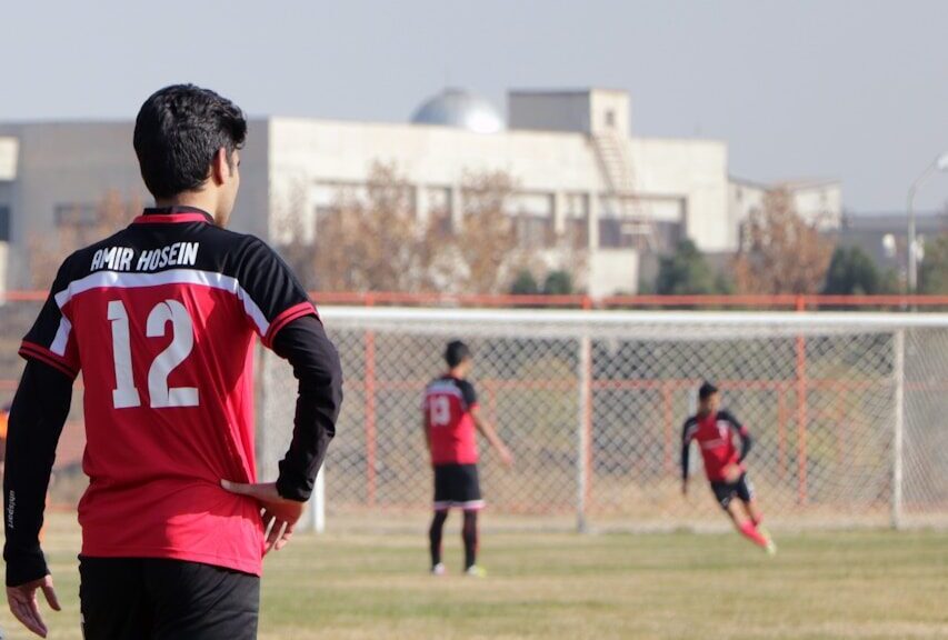 man in blue and red soccer jersey shirt and black shorts standing on green grass field