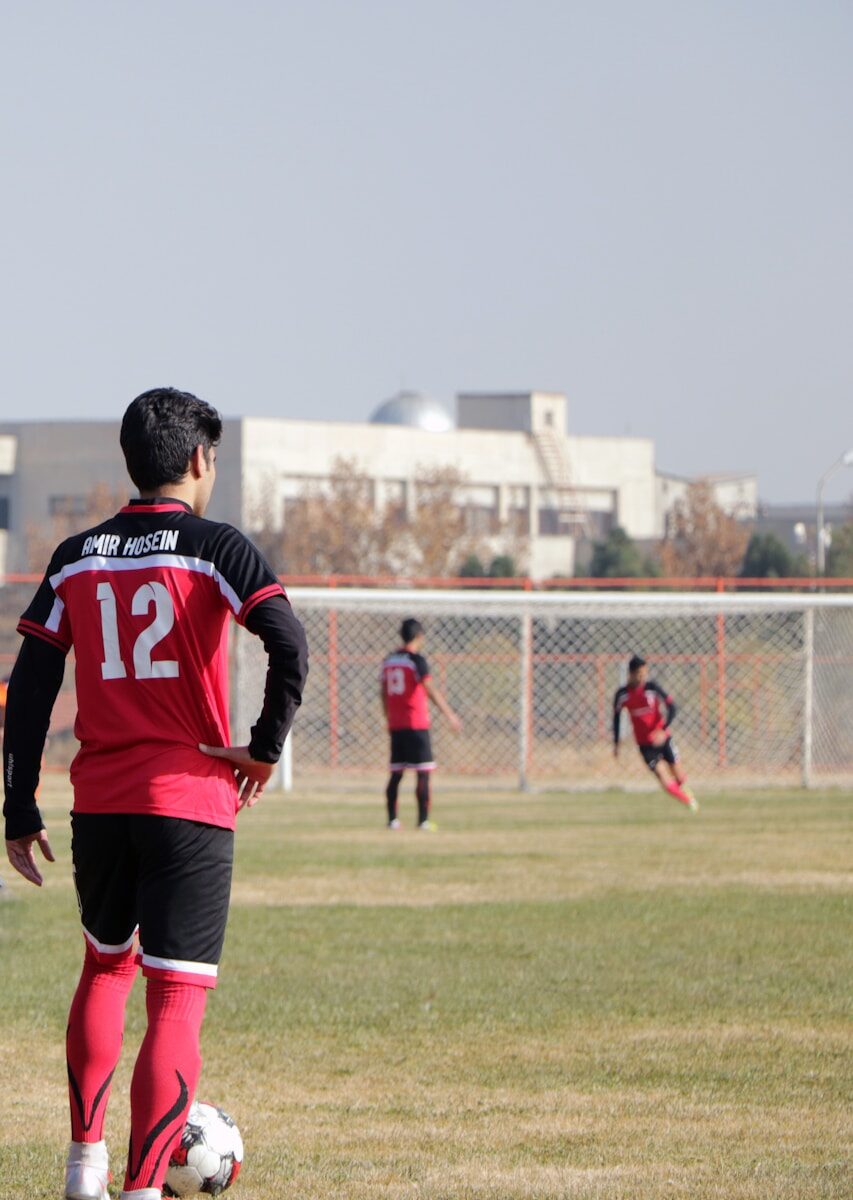 man in blue and red soccer jersey shirt and black shorts standing on green grass field
