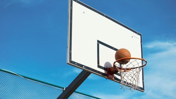 A basketball scoring shot on an outdoor court with a clear blue sky backdrop.