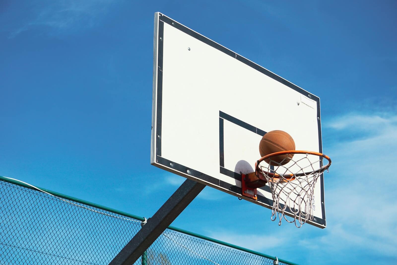 A basketball scoring shot on an outdoor court with a clear blue sky backdrop.
