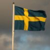 The Swedish flag waves on a flagpole in Jönköping, Sweden, framed by storm clouds.