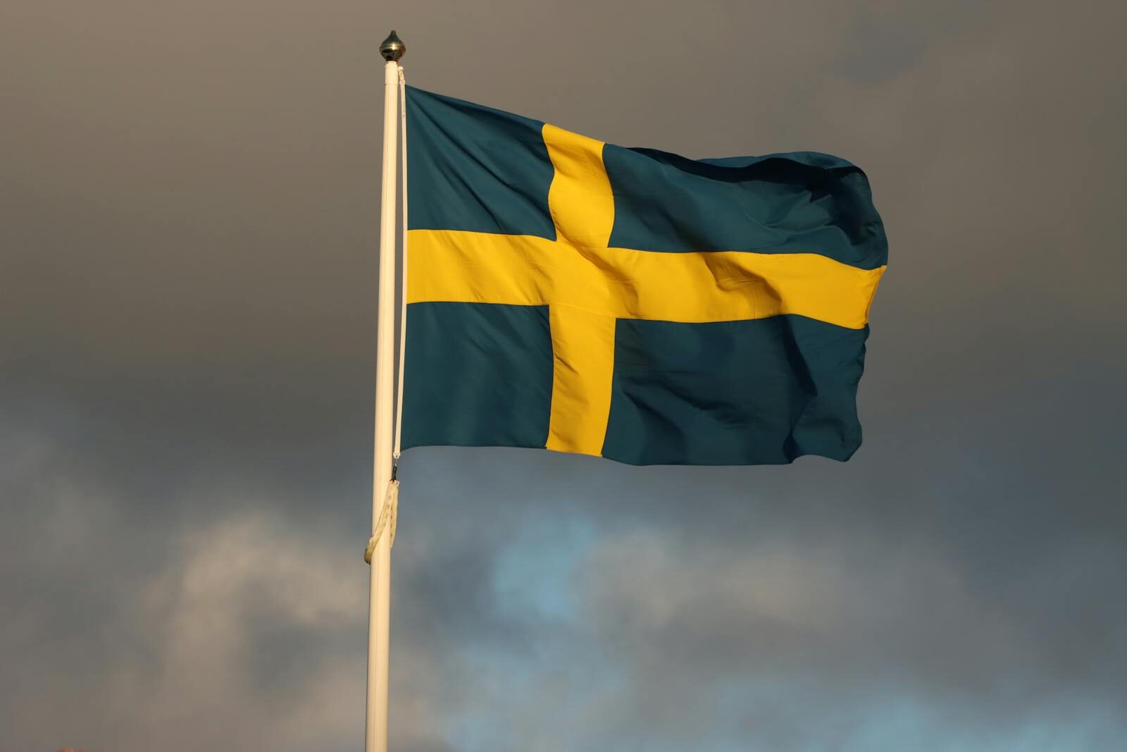The Swedish flag waves on a flagpole in Jönköping, Sweden, framed by storm clouds.
