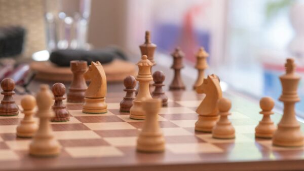 Close-up of a strategic chess game on a wooden chessboard indoors, showcasing knights, bishops, and pawns.