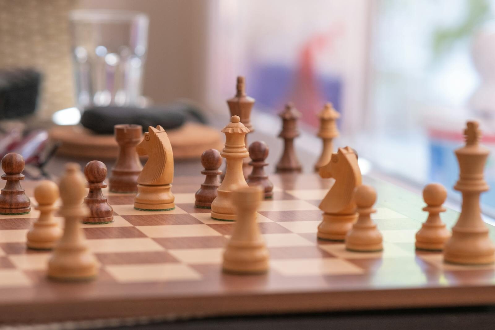 Close-up of a strategic chess game on a wooden chessboard indoors, showcasing knights, bishops, and pawns.