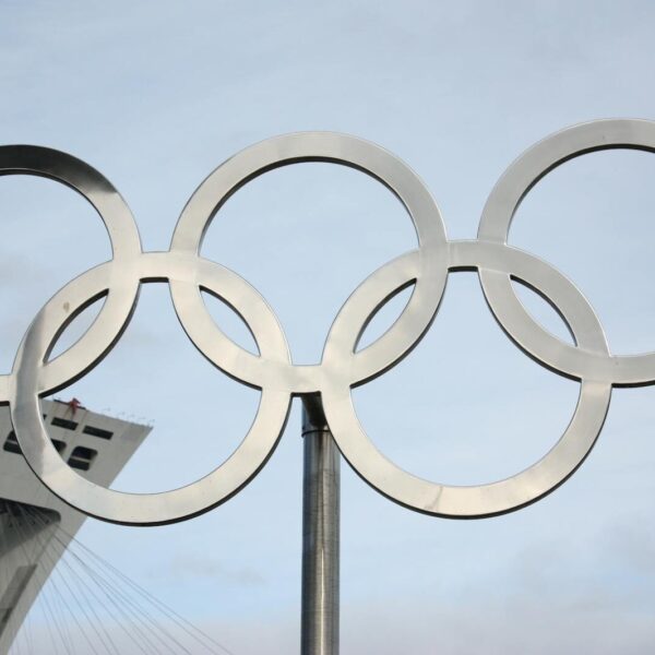 The iconic Olympic rings in front of a tall structure on a clear day.