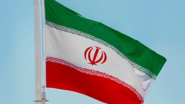 Low-angle view of the Iranian flag waving on a flagpole against a clear blue sky in Tehran, Iran.