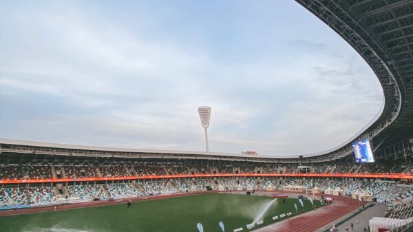 Wide-angle view of a modern stadium in Minsk with sprinklers on the field at dusk.
