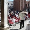 Busy outdoor cafe in Piazza San Marco, Venice with waiters in white jackets serving guests.