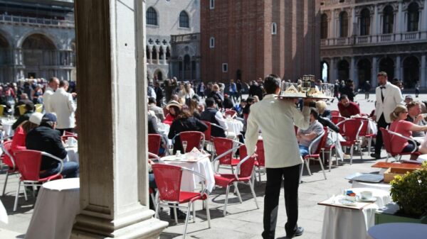 Busy outdoor cafe in Piazza San Marco, Venice with waiters in white jackets serving guests.