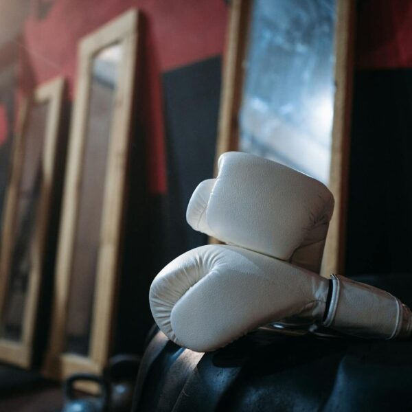 Close-up of white boxing gloves on gym equipment with mirrors reflecting in the background.