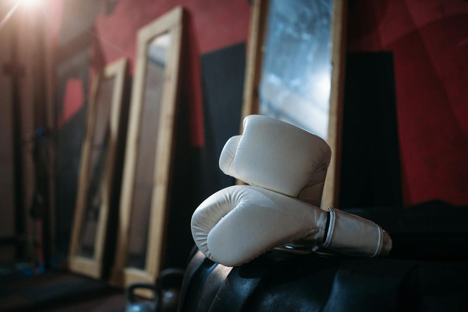 Close-up of white boxing gloves on gym equipment with mirrors reflecting in the background.