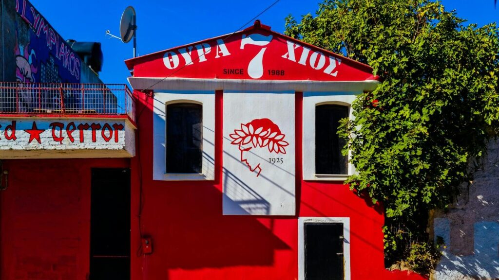Colorful urban building in Chios with red facade and artistic mural under blue sky.