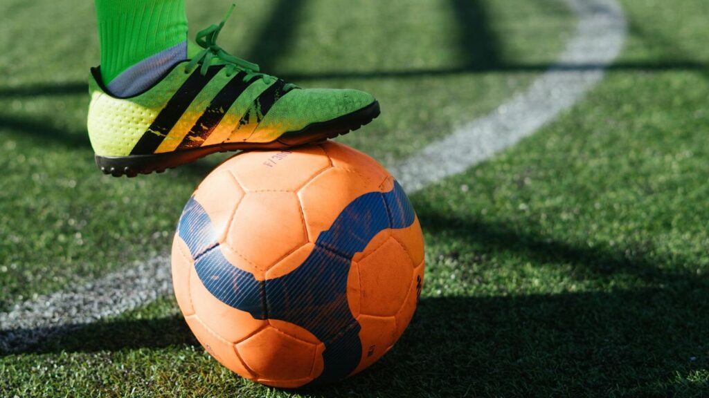 Dynamic shot of a soccer player's foot on a vivid orange ball on a lush green field.