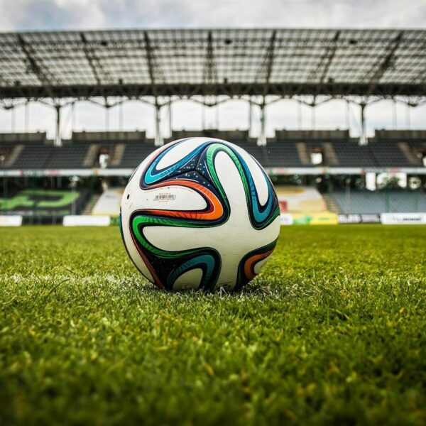 A vibrant soccer ball rests on a lush green field inside an empty stadium, capturing the essence of sports.