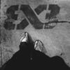 Black and white of crop unrecognizable person in dark outfit and flip flops standing on asphalt road with graffiti
