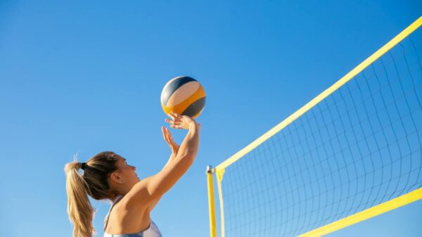 A woman plays volleyball on a sunny day, reaching to hit the ball over the net.