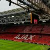 A wide view of the interior of Ajax stadium in Amsterdam, showcasing the iconic red seats and green field.