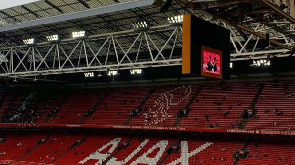 A wide view of the interior of Ajax stadium in Amsterdam, showcasing the iconic red seats and green field.